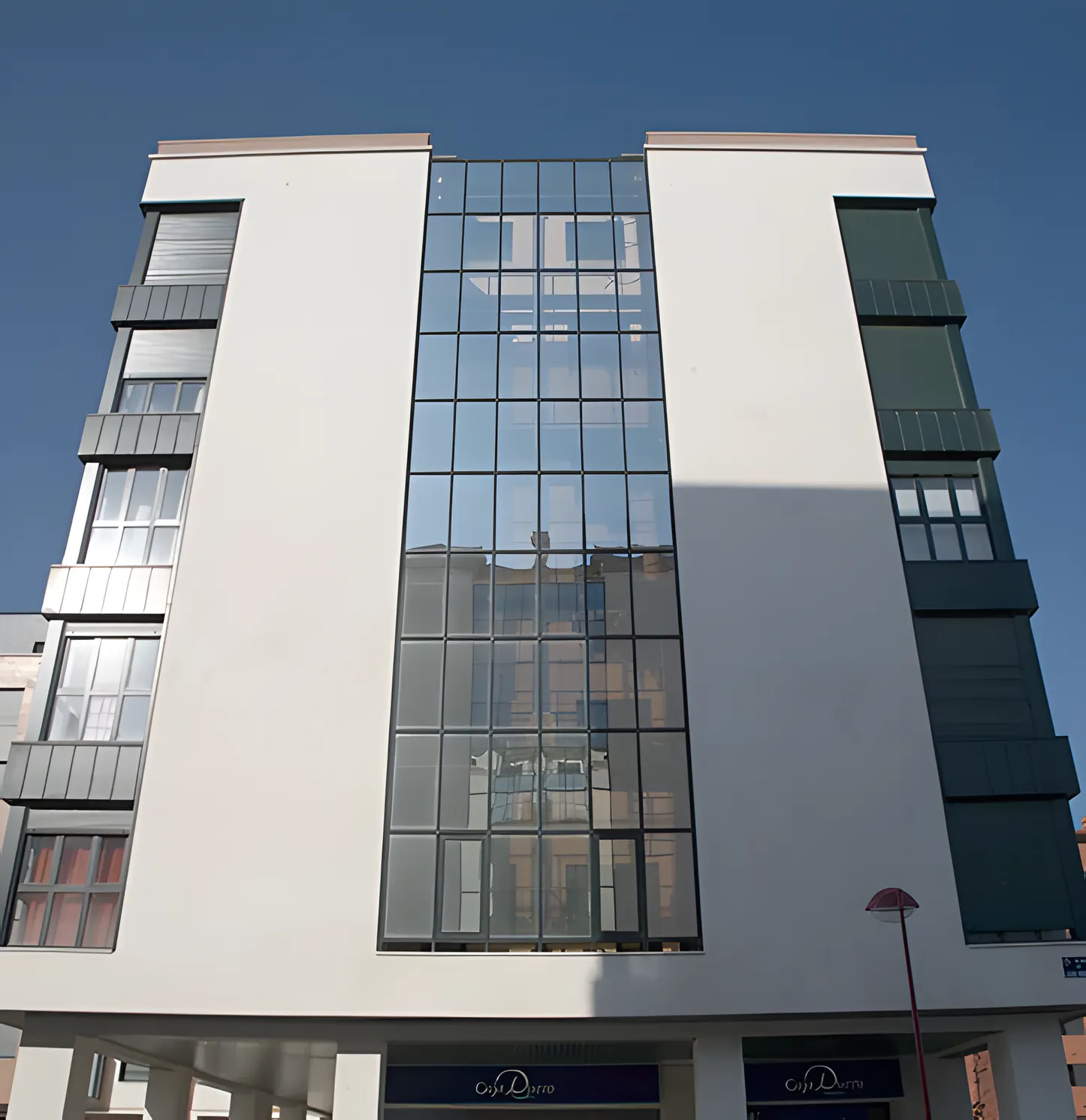 Edificio de viviendas con un cuerpo central de muro cortina entre paños blancos