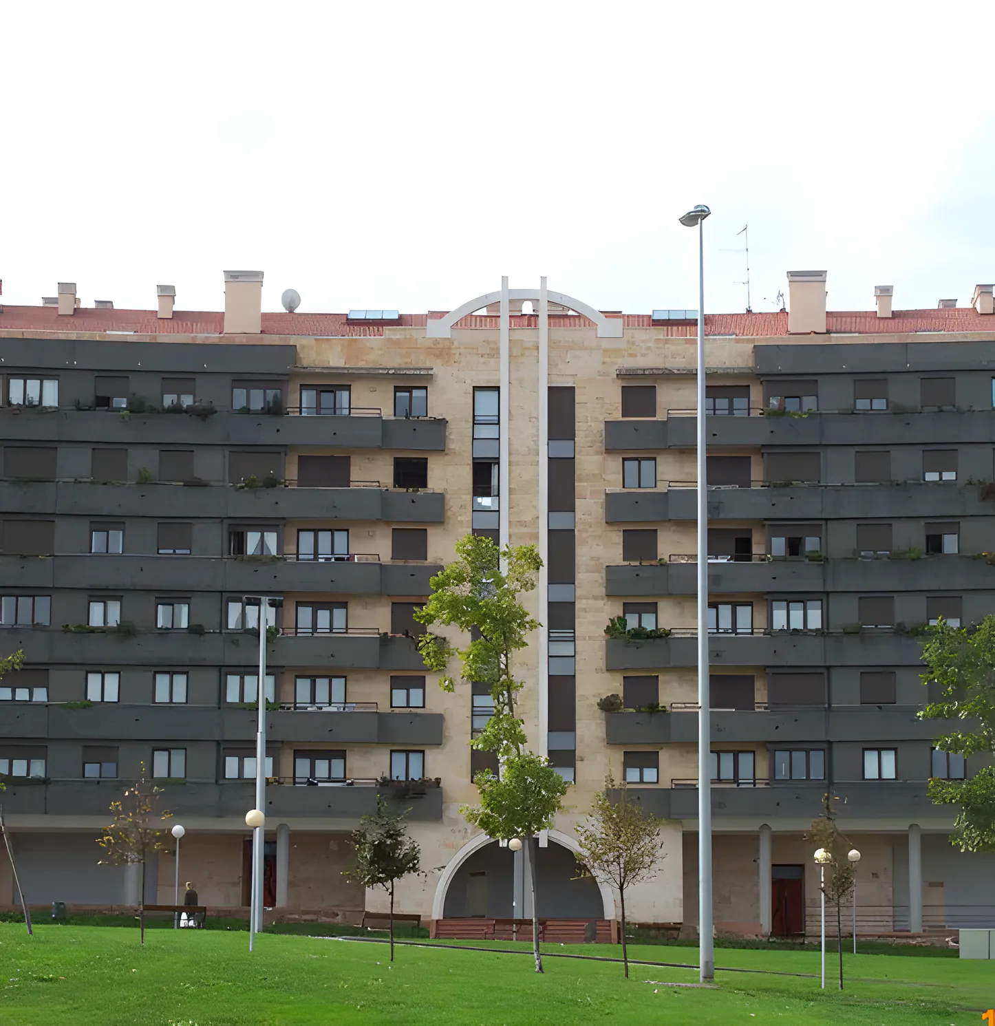 Conjunto residencial de ladrillo con terrazas y carpintería oscura, frente a un jardín